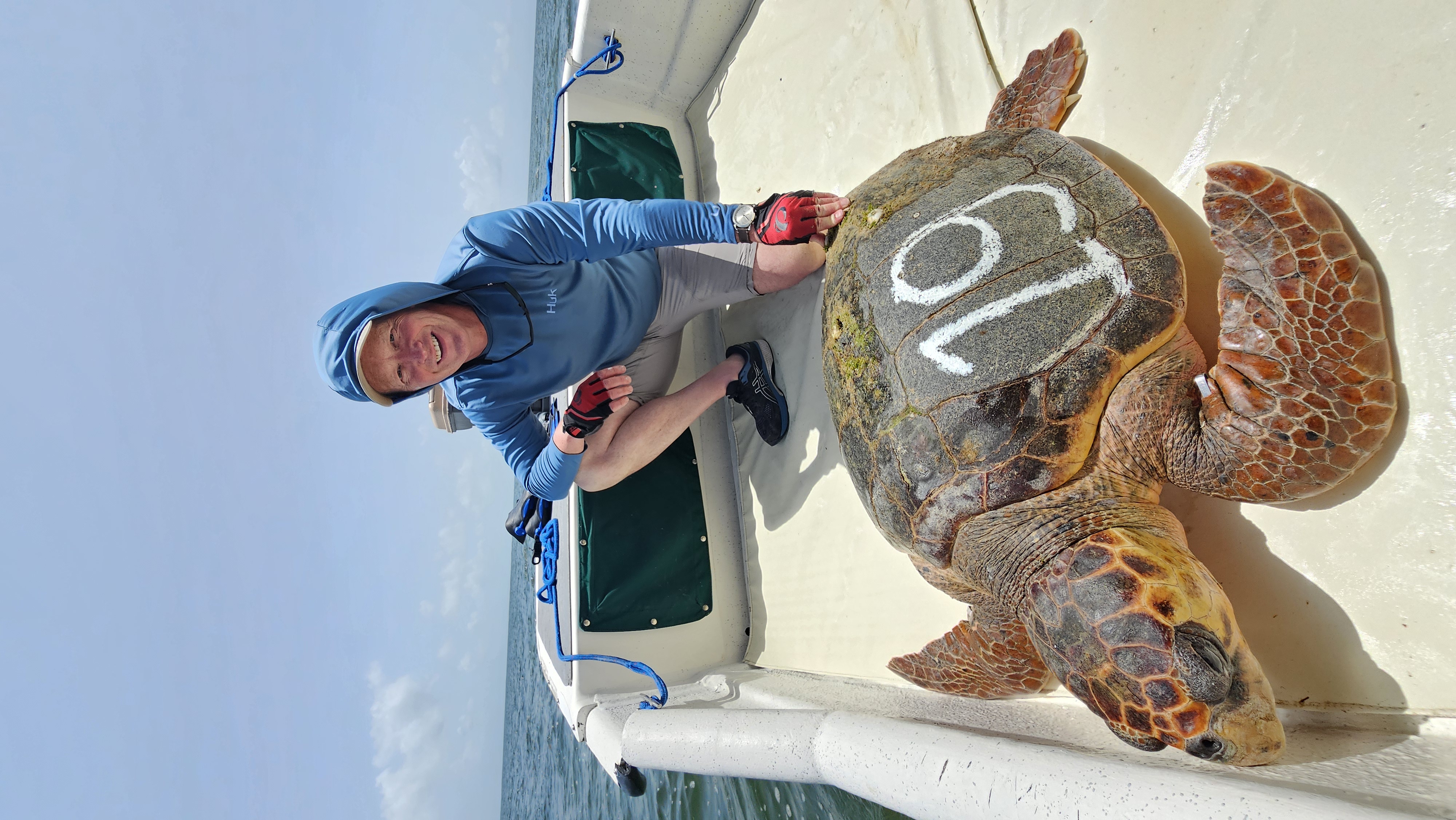 Researcher posing with a large loggerhead sea turtle marked with the number 19 on its carapace